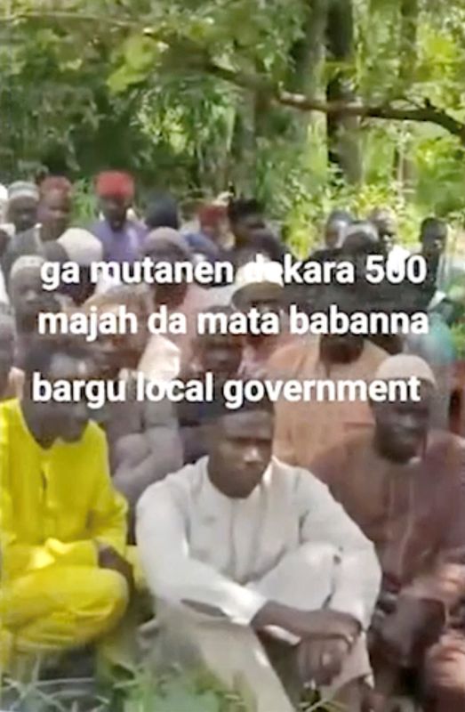 Abducted women, children, and older people sitting on grass in a social media video from an armed group in Nigeria's Niger State.
