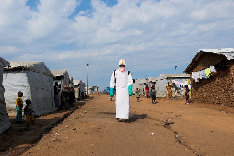 Health worker in full personal protective equipment disinfecting an area during the burial of suspected Ebola victims at a displaced persons camp in Bunia, Democratic Republic of Congo.